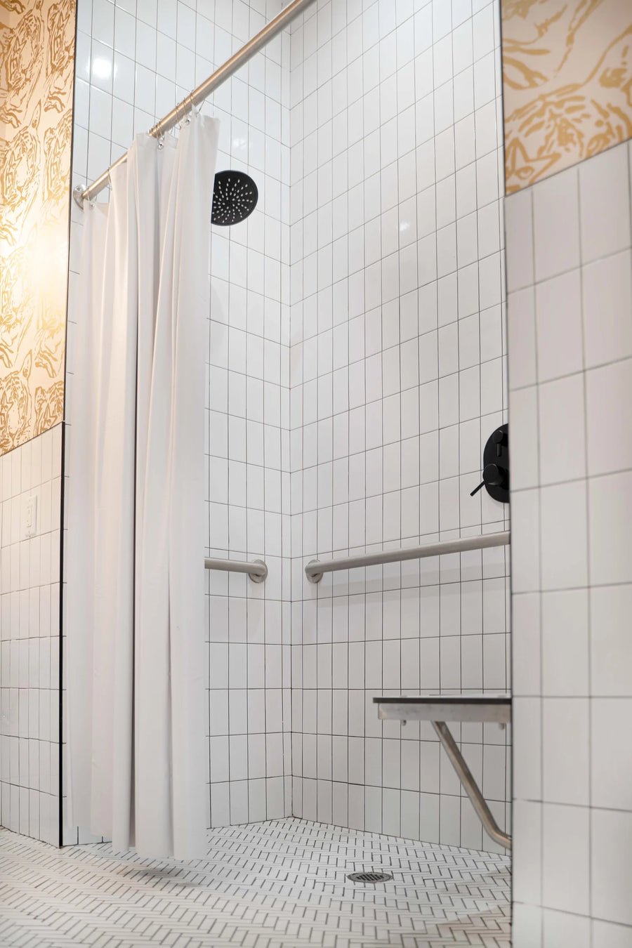 A modern white tiled shower stall with a white curtain, metal grab bars, a built-in bench, and a circular showerhead, shown in a clean interior view.